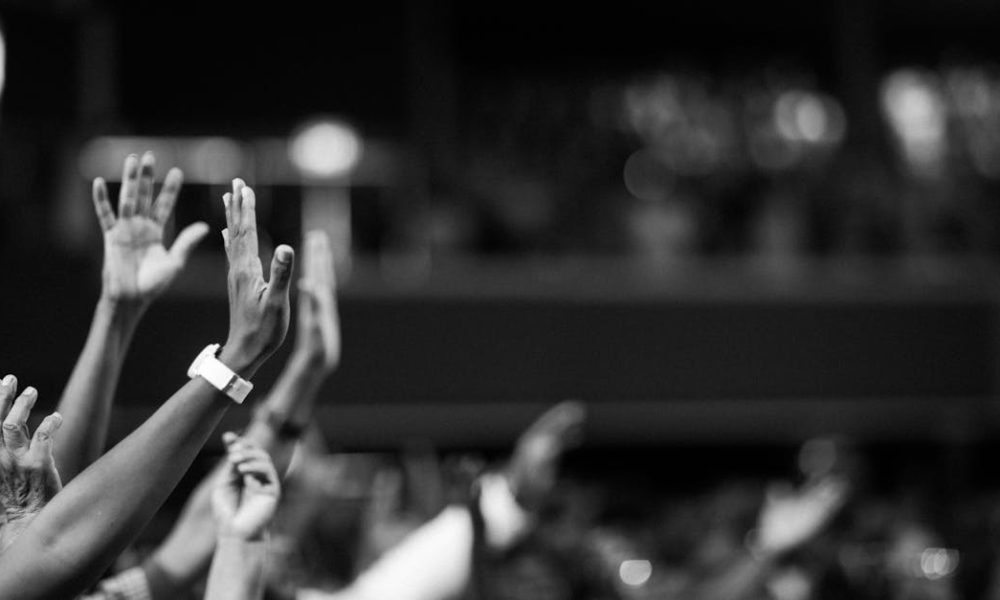 Black and white image of audience with hands raised, capturing concert energy.